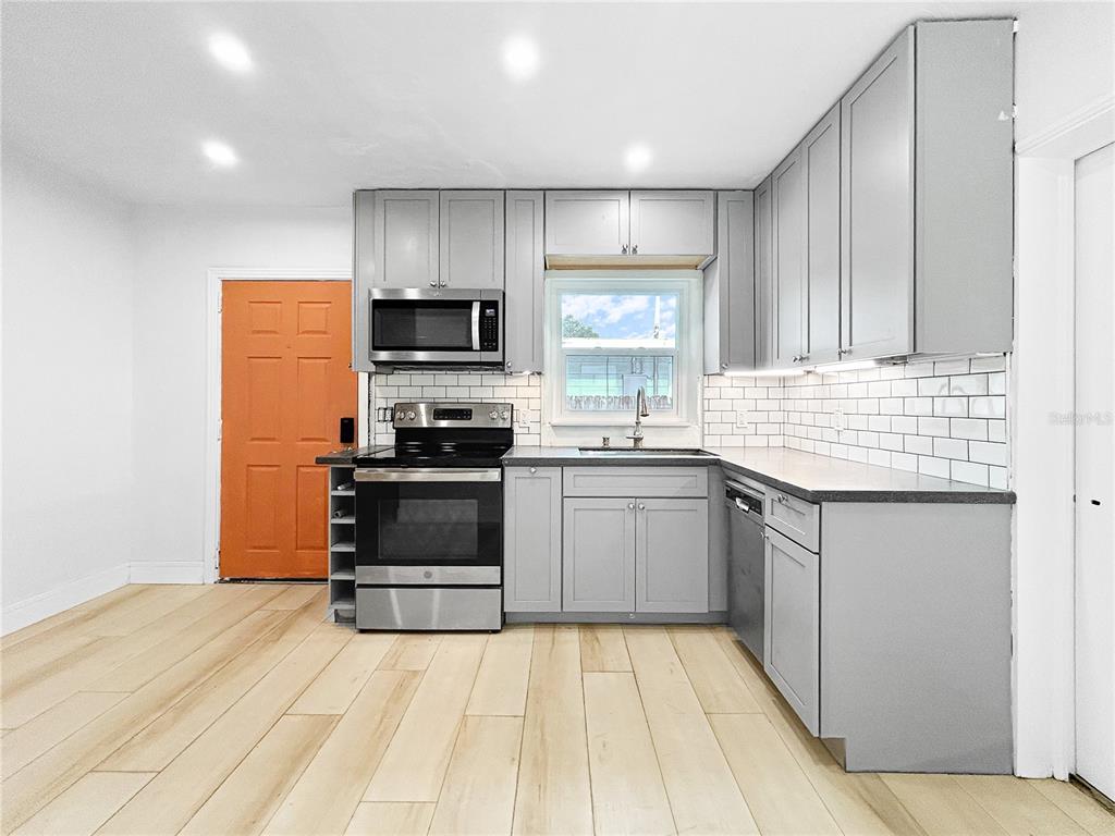A kitchen features gray cabinets, stainless steel appliances, white subway tile backsplash, and light wood flooring — 5021 9TH AVENUE S, GULFPORT, FL