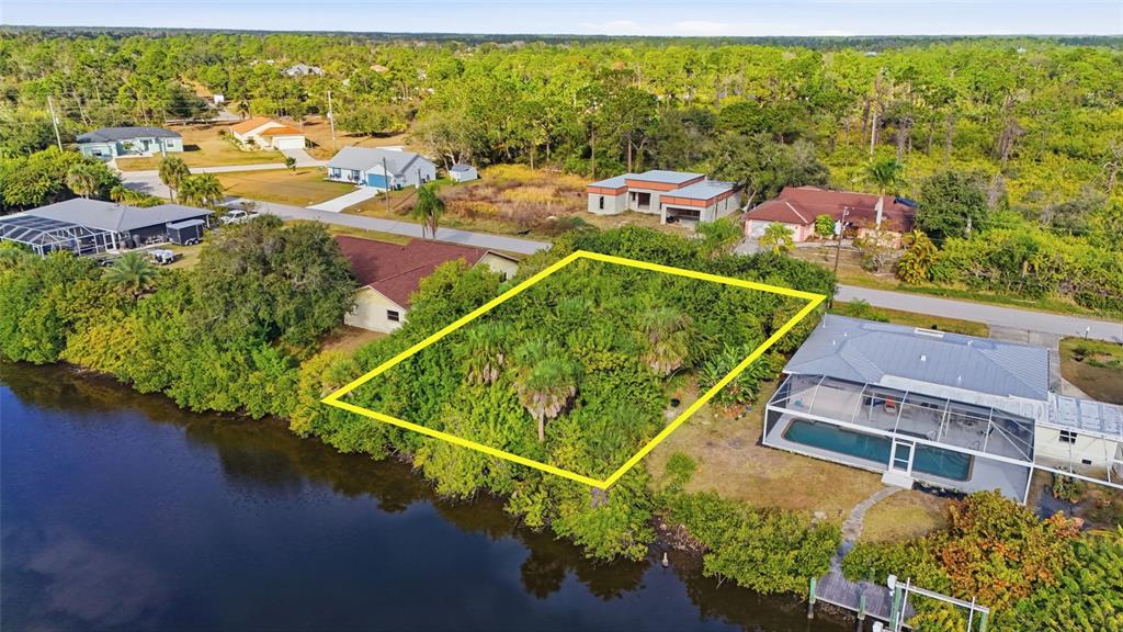 An aerial view shows a vacant, wooded waterfront lot outlined in yellow between two houses — 12309 MITCHELL TERRACE, PORT CHARLOTTE, FL