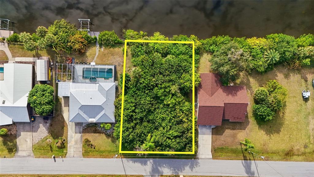 An aerial view shows a vacant, tree-covered rectangular lot situated between two houses near water — 12309 MITCHELL TERRACE, PORT CHARLOTTE, FL