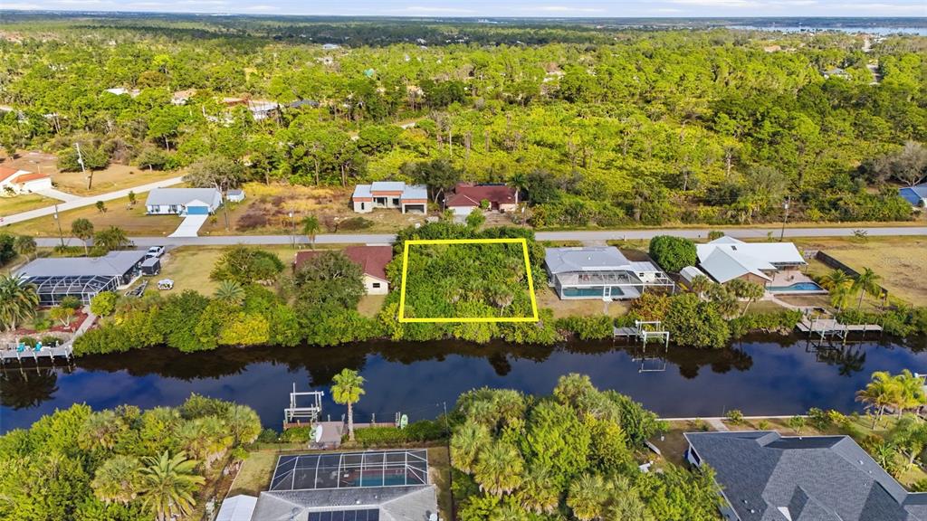 An aerial view shows a vacant, wooded waterfront lot highlighted by a yellow border — 12309 MITCHELL TERRACE, PORT CHARLOTTE, FL