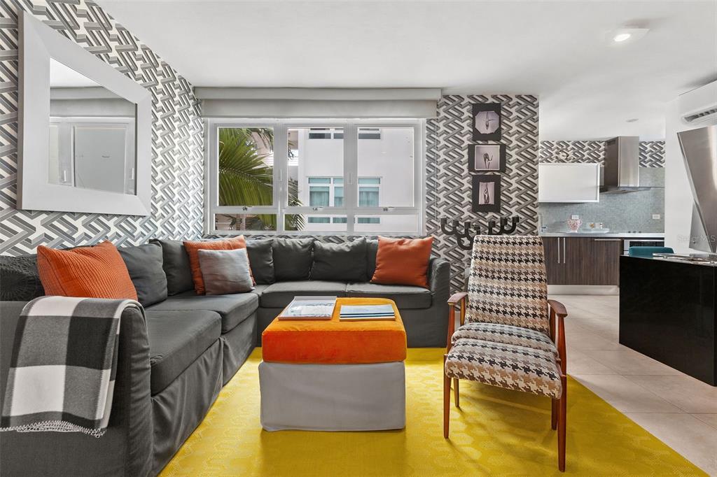 A living room features a grey sectional sofa, orange accents, patterned wallpaper, and a yellow rug — 59 CALLE SAN MIGUEL UNIT 303, SAN JUAN, PR