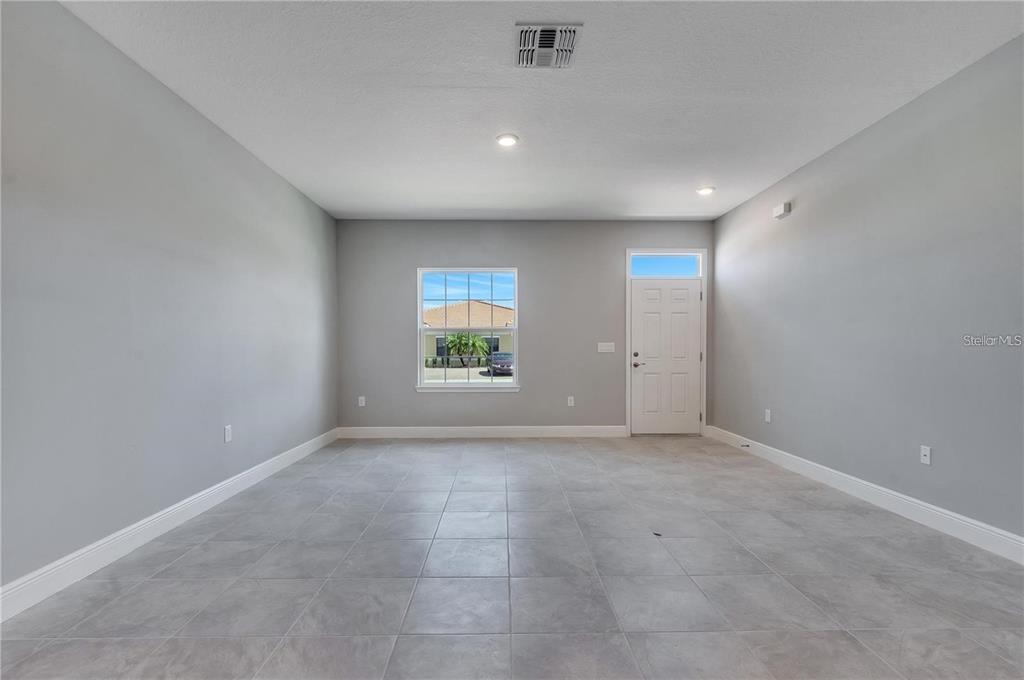 An empty room features gray walls, light-colored tile flooring, a window, and a white door — 1799 CORIANDER DRIVE UNIT 1799, KISSIMMEE, FL