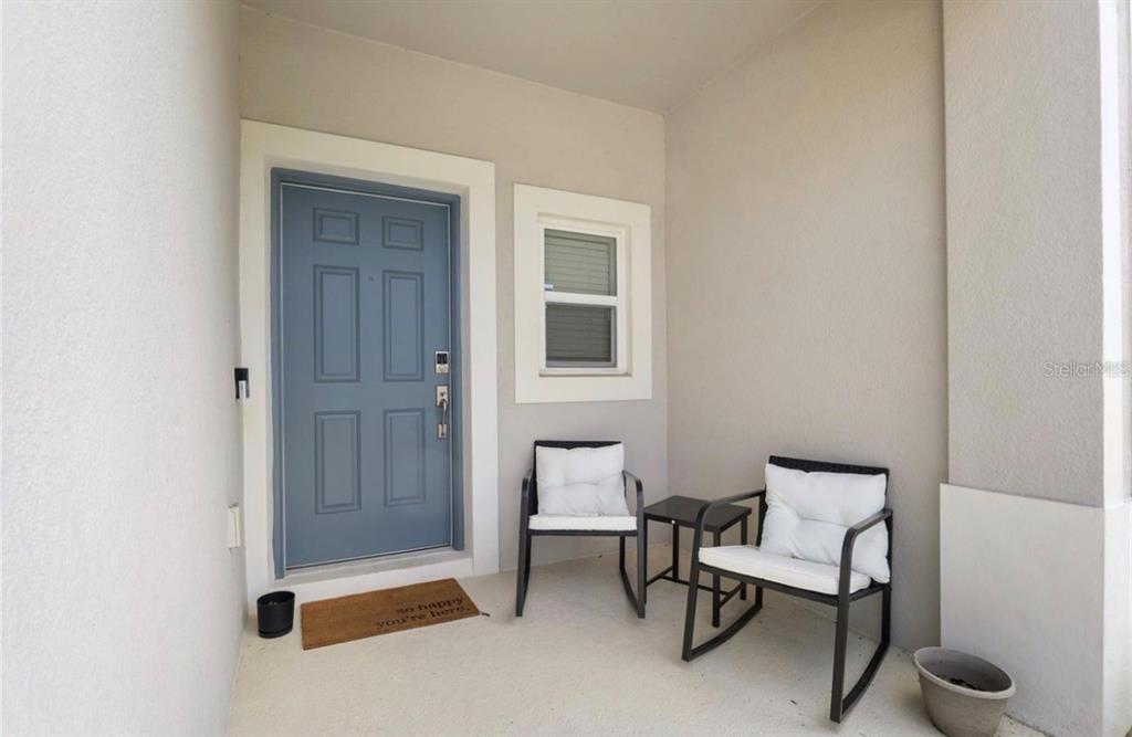A covered front porch features a blue door, two chairs, and a small side table — 4840 REVOLUTIONARY WAY, ST CLOUD, FL