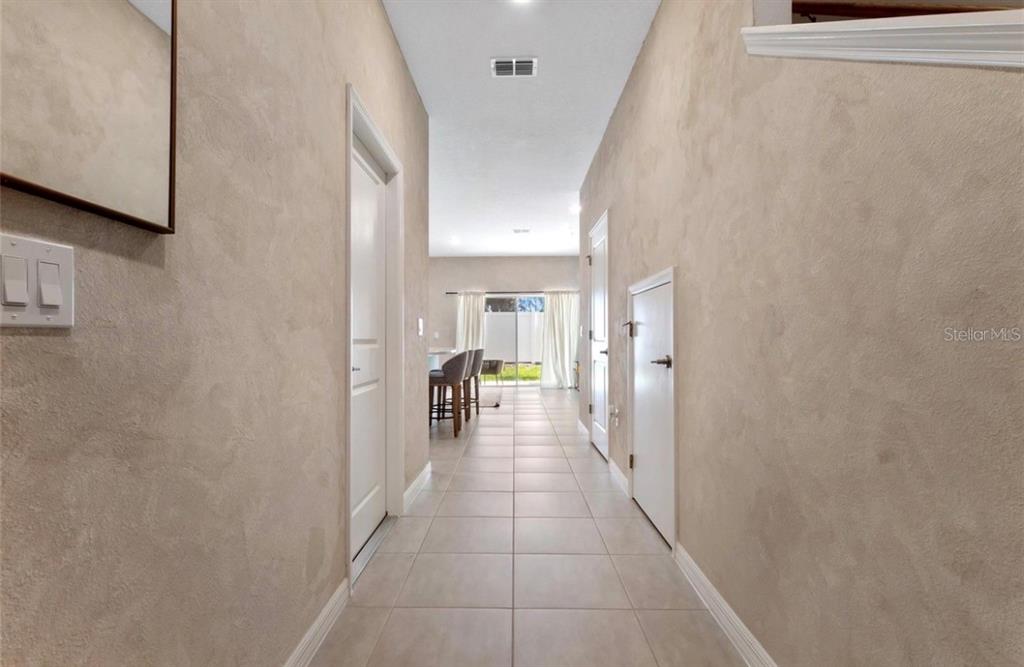 A tiled hallway leads from the foreground toward an open living area with glass doors — 4840 REVOLUTIONARY WAY, ST CLOUD, FL