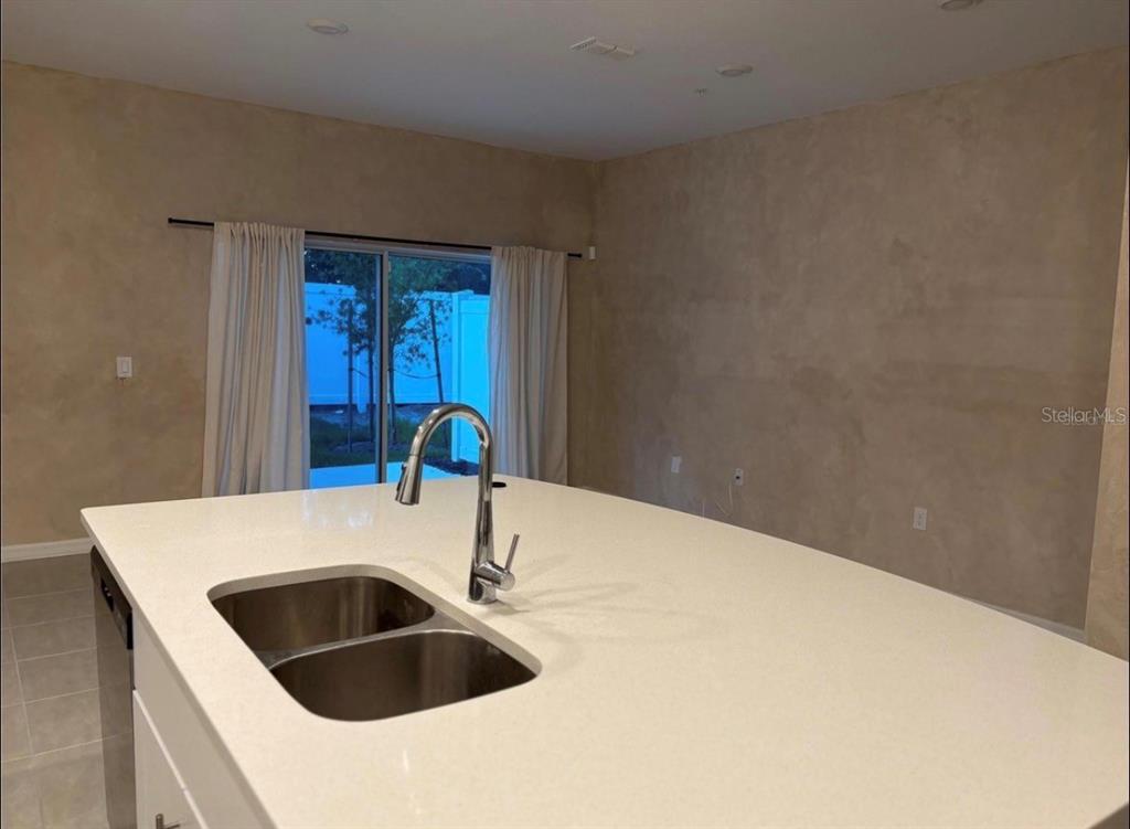 A kitchen island with a double sink and faucet sits before a sliding glass door — 4840 REVOLUTIONARY WAY, ST CLOUD, FL