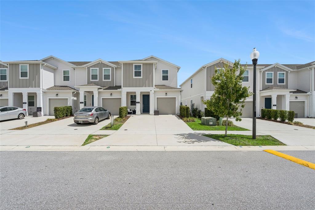 A row of two-story townhomes with attached garages and concrete driveways under a clear sky — 7629 DANUBE ROAD, KISSIMMEE, FL