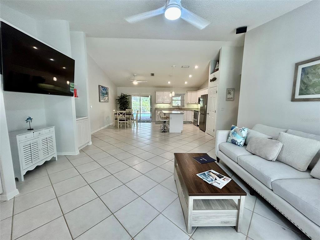 A bright, open-concept living room and kitchen area features white tile flooring and vaulted ceilings — 142 SOLANA STREET, NORTH PORT, FL