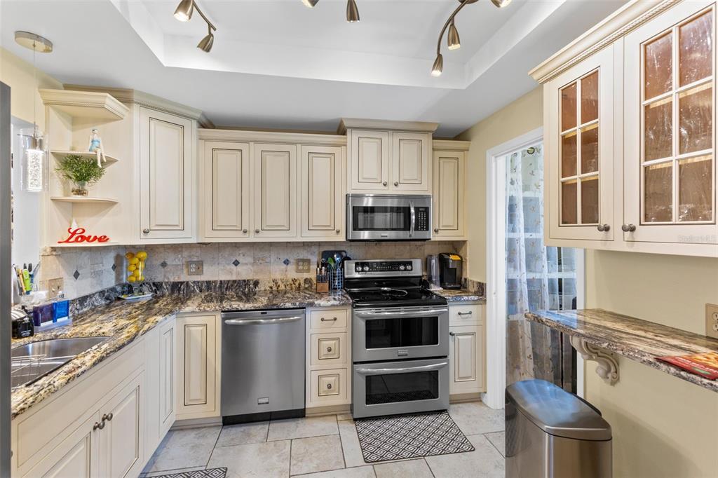A kitchen features cream cabinets, granite countertops, stainless steel appliances, and tile flooring — 924 VIRGINIA AVENUE, ST CLOUD, FL