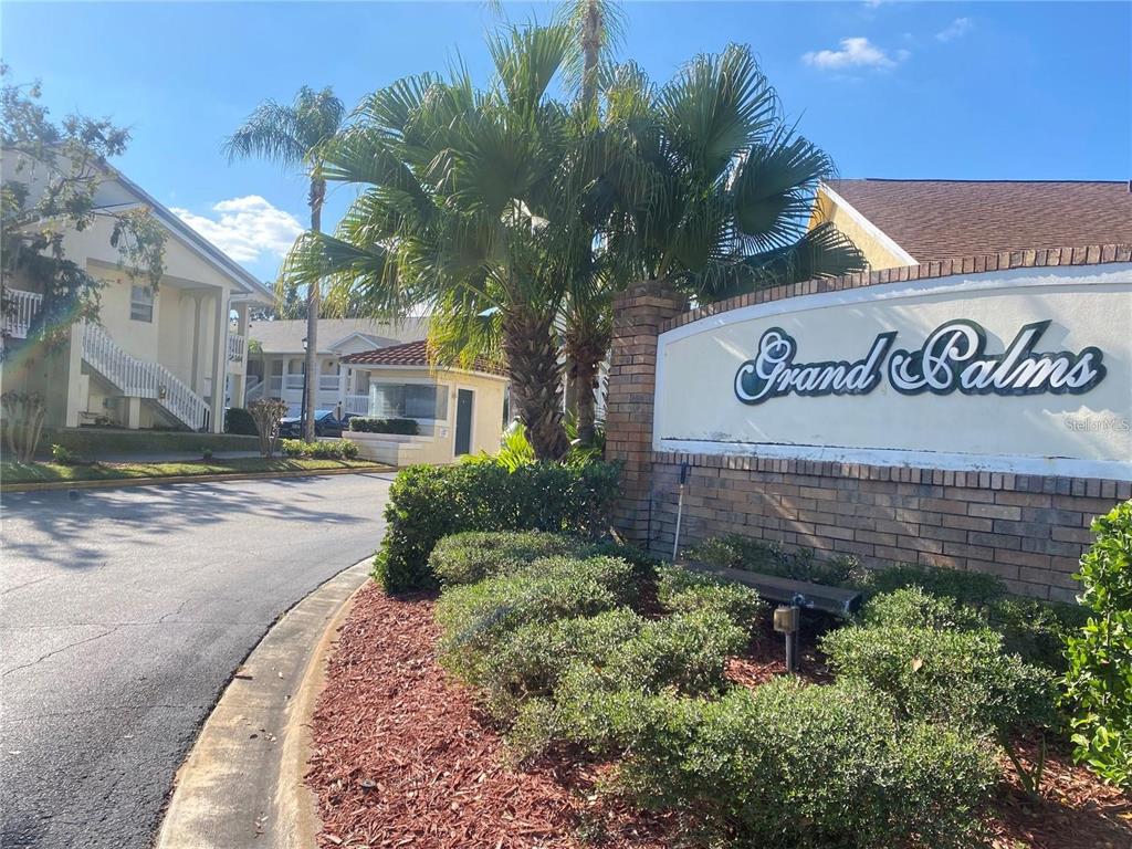 A brick sign for Grand Palms stands near a palm tree and apartment buildings — 3204 SABAL PALMS COURT UNIT B, KISSIMMEE, FL