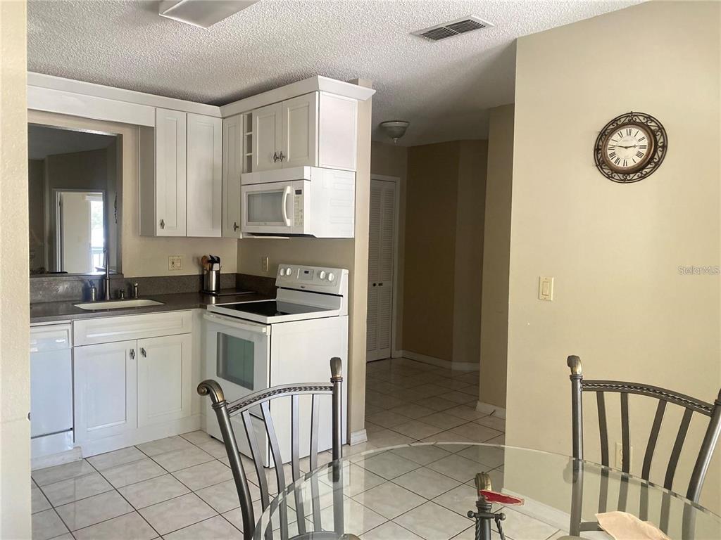 A kitchen features white cabinets, white appliances, and tile flooring next to a dining area — 3204 SABAL PALMS COURT UNIT B, KISSIMMEE, FL