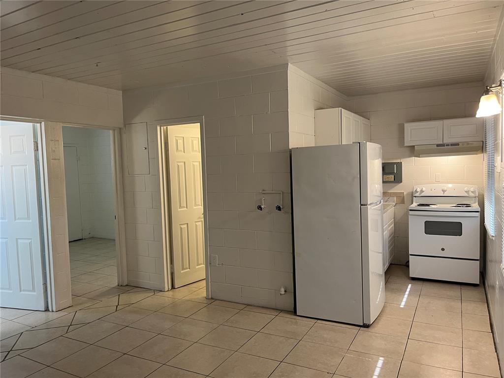A kitchen with white appliances, tile flooring, and a block wall interior — 709 BOSTON AVENUE, ORLANDO, FL