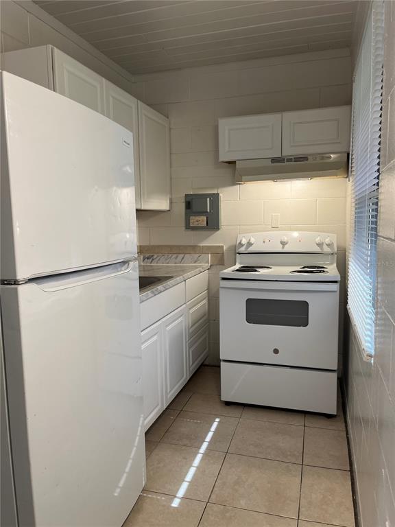 A small kitchen features white appliances, white cabinets, tiled floors, and exposed concrete block walls — 709 BOSTON AVENUE, ORLANDO, FL