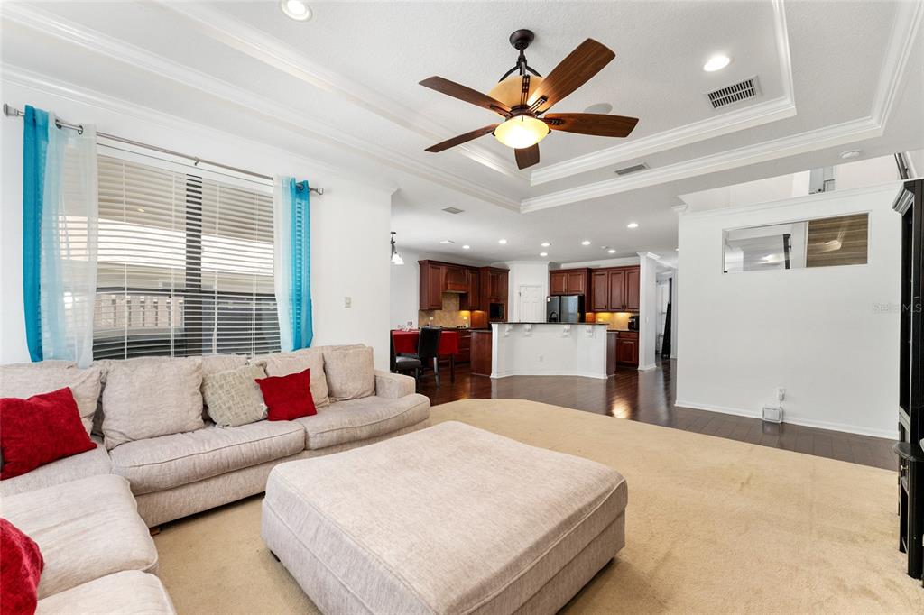 A living room with beige carpet and a sectional sofa opens to a dark wood kitchen — 4444 NW 82ND ROAD, GAINESVILLE, FL