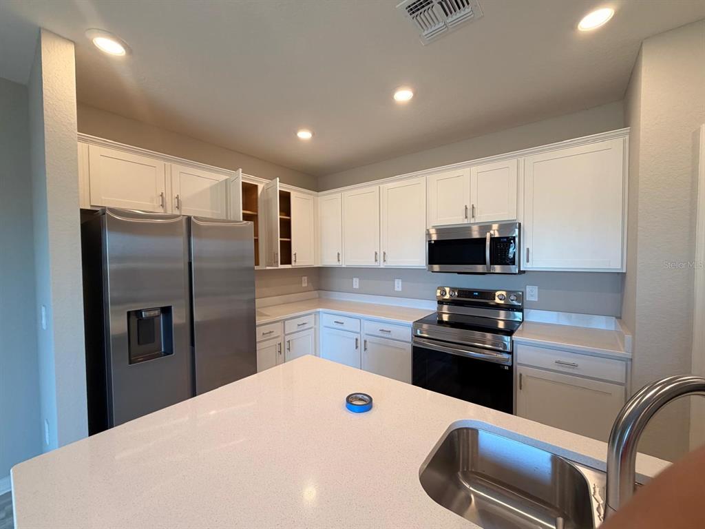 A kitchen features white cabinets, stainless steel appliances, and a white quartz-topped island — 5117 SYLAS JAX AVENUE, WINTER HAVEN, FL