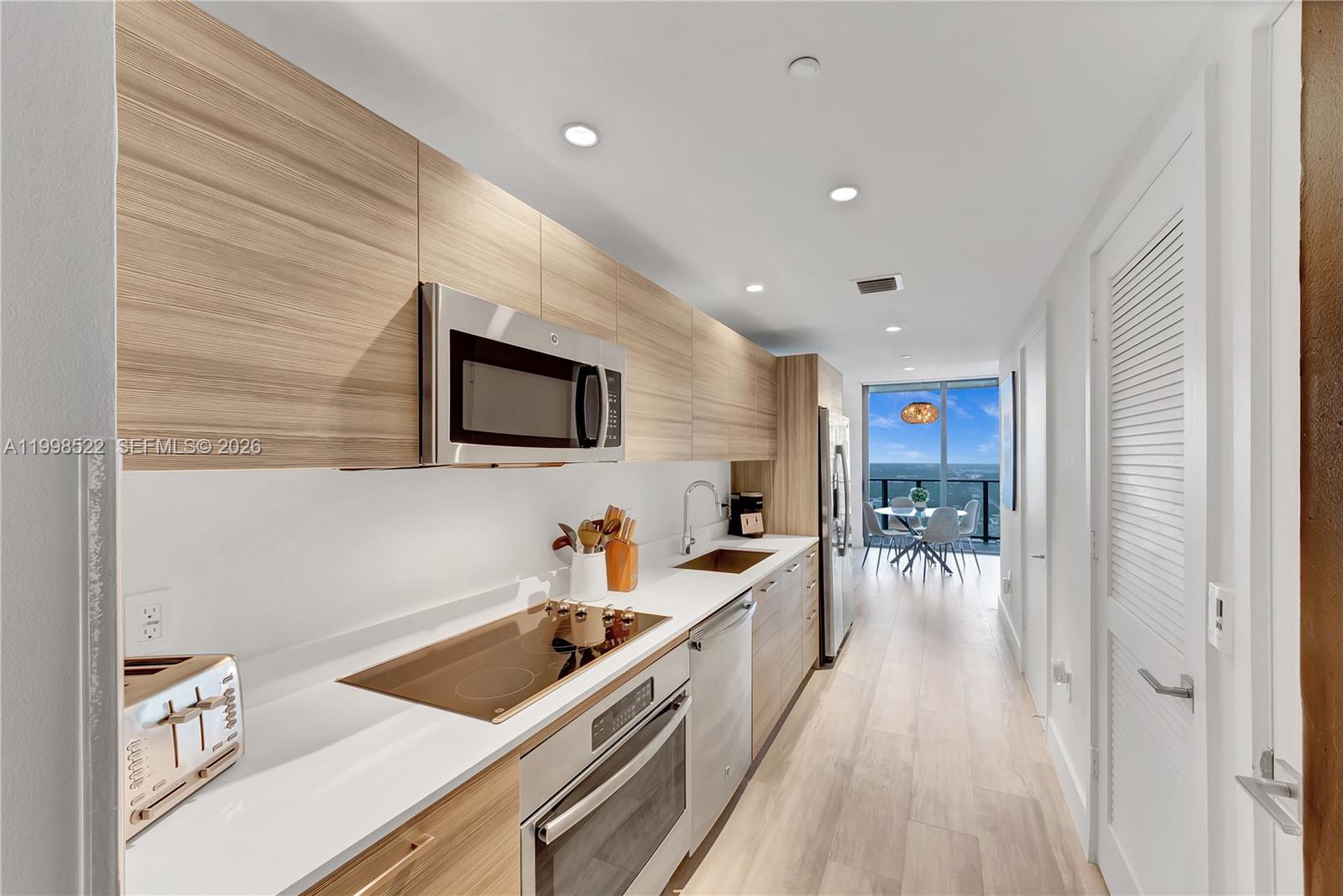 A modern galley kitchen features light wood cabinetry, stainless steel appliances, and a view of the ocean — 121 NE 34th St # 2815, Miami FL 33137, MIAMI, FL