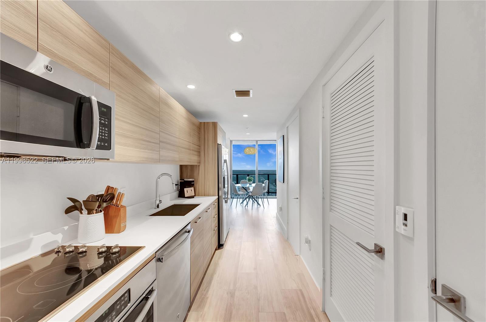 A galley kitchen features light wood cabinets, white countertops, and a view of the ocean — 121 NE 34th St # 2815, Miami FL 33137, MIAMI, FL