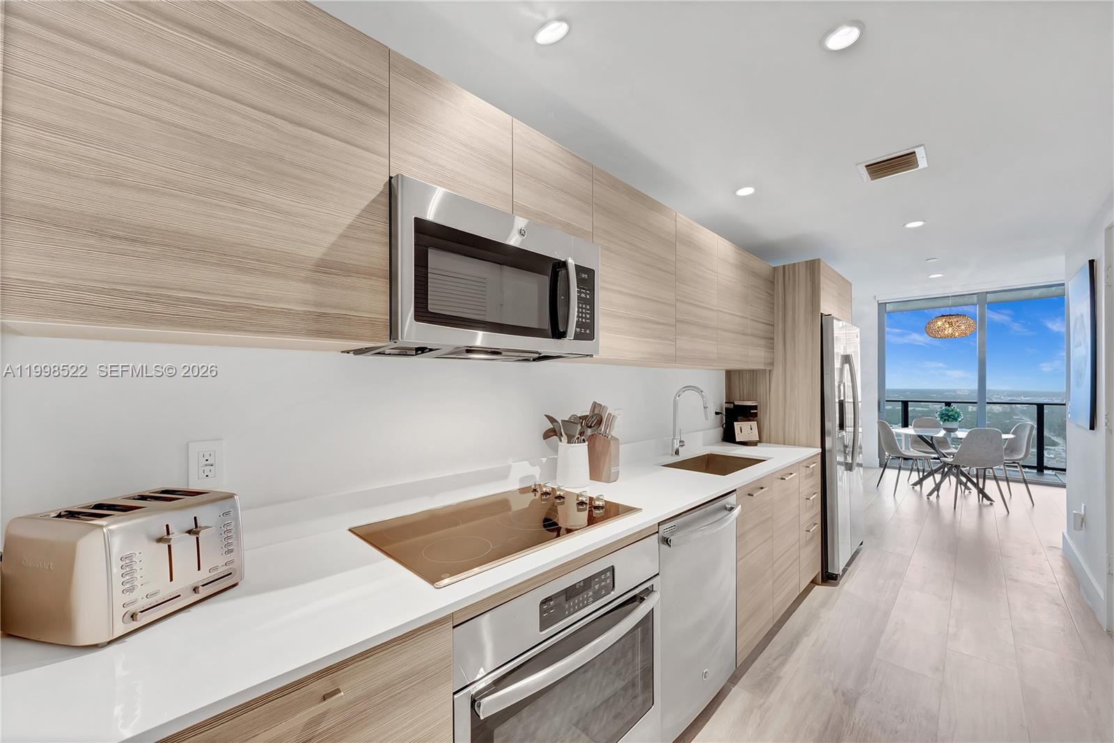 A modern kitchen features light wood cabinetry, stainless steel appliances, and a view of the ocean — 121 NE 34th St # 2815, Miami FL 33137, MIAMI, FL