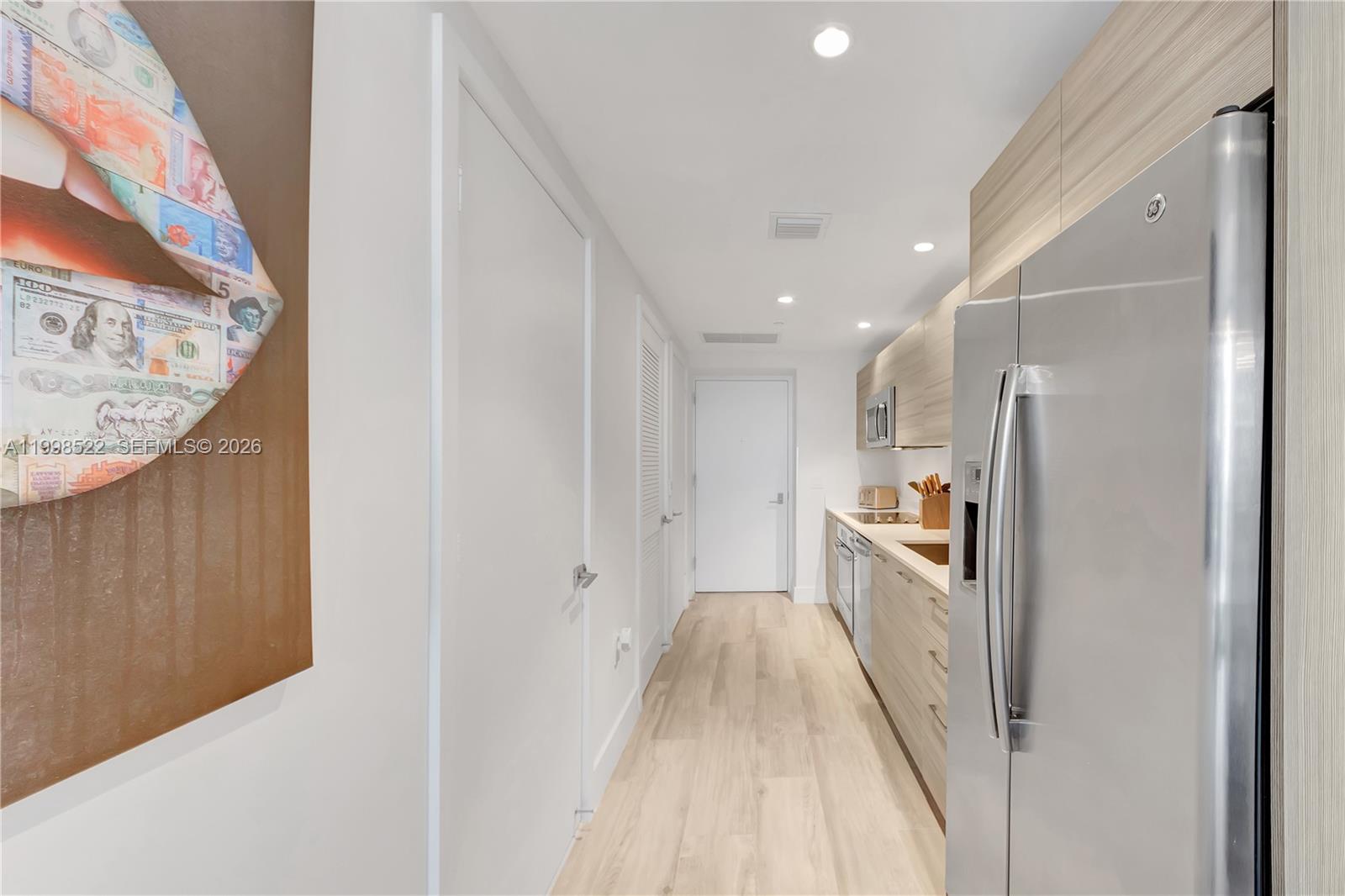 A galley kitchen features light wood cabinetry, stainless steel appliances, and light-colored wood flooring — 121 NE 34th St # 2815, Miami FL 33137, MIAMI, FL