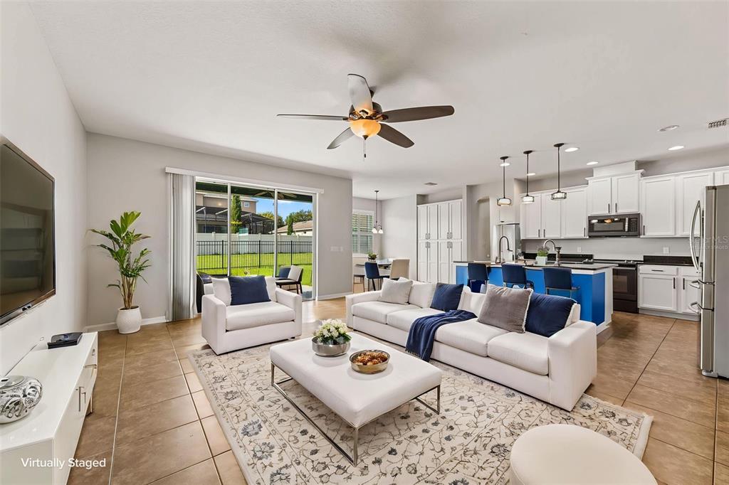 This open-concept living room features tile flooring, a kitchen with blue cabinetry, and sliding glass doors — 2100 MISTY GLEN DRIVE, APOPKA, FL