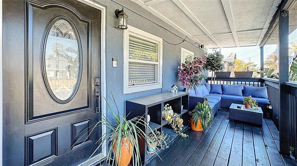 A covered porch features a black front door, a shelving unit, and outdoor lounge furniture — 1201 W 12TH STREET, SANFORD, FL