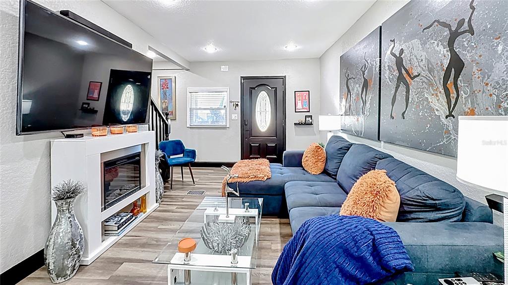 A living room features a large television, fireplace, blue sectional sofa, and abstract wall art — 1201 W 12TH STREET, SANFORD, FL