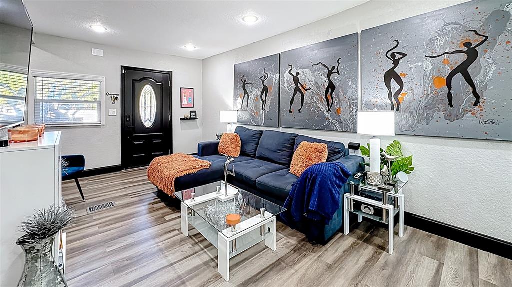 A living room features a blue sectional sofa, a glass coffee table, and abstract wall art — 1201 W 12TH STREET, SANFORD, FL