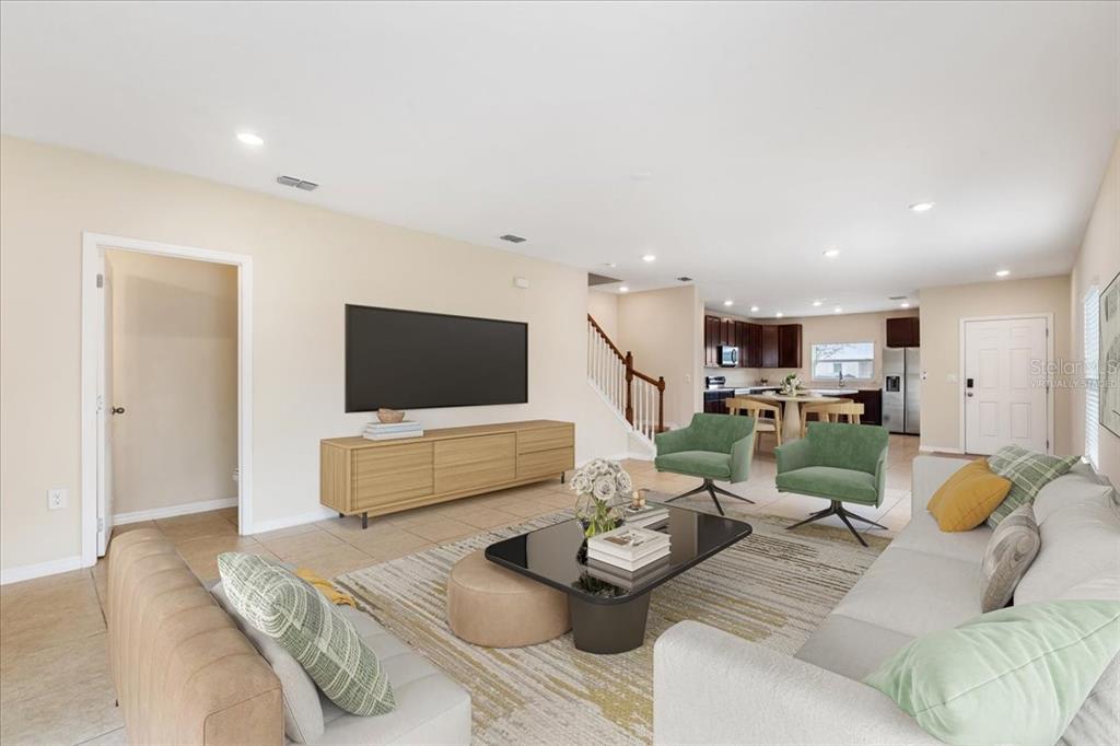 This living room features tile flooring, a wall-mounted television, and an open-concept kitchen — 4855 CORAL CASTLE DRIVE, KISSIMMEE, FL