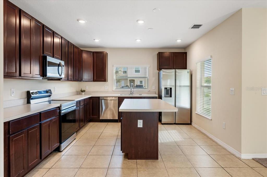 A kitchen features dark wood cabinets, stainless steel appliances, a center island, and tile flooring — 4855 CORAL CASTLE DRIVE, KISSIMMEE, FL