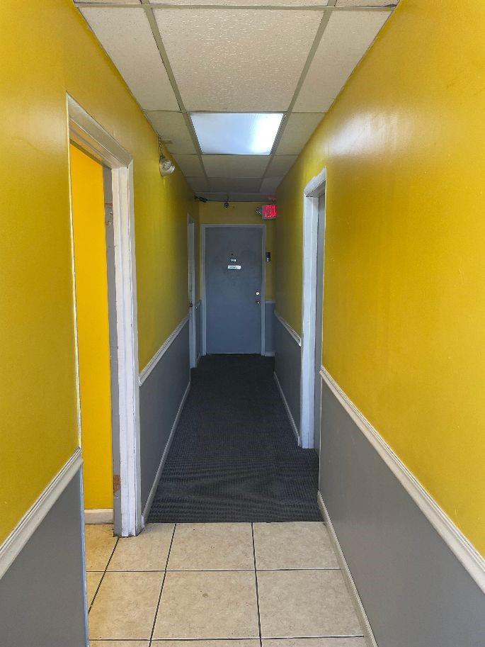 A narrow hallway features yellow walls, gray wainscoting, a tiled floor, and a gray door — 1075 Sunset Strip, Sunrise FL 33313, SUNRISE, FL