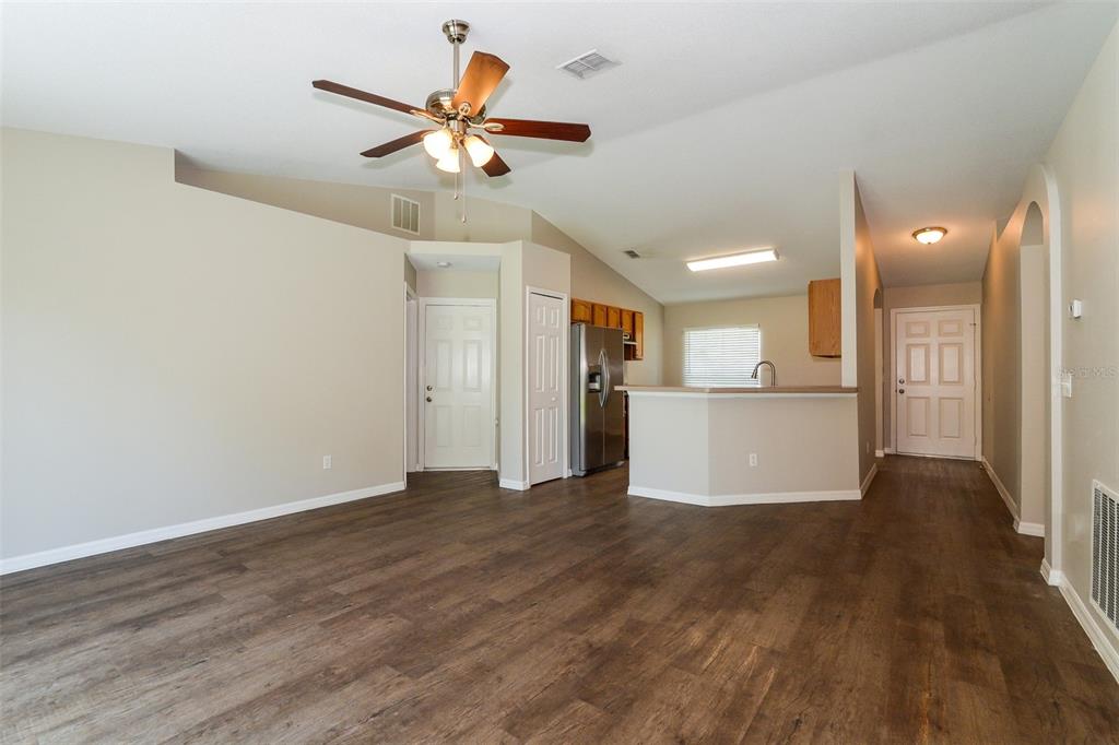 An open-concept living area features wood-look flooring, a ceiling fan, and an adjacent kitchen — 2783 S SLATER DRIVE, DELTONA, FL