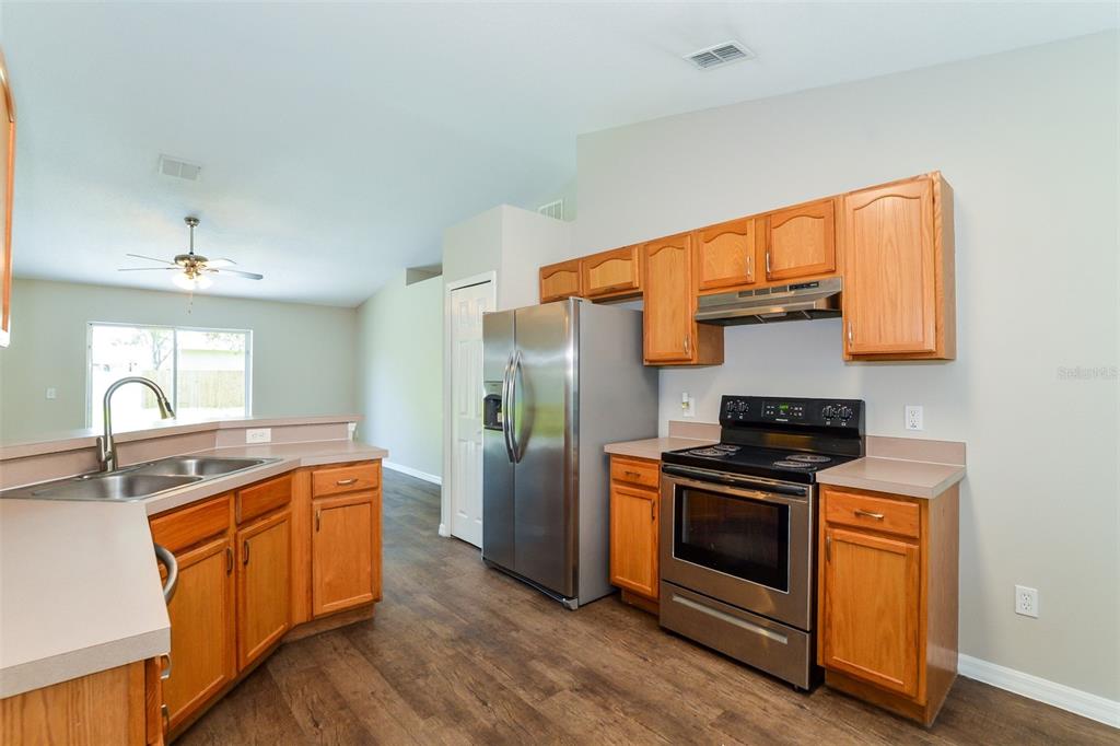 A kitchen with wood cabinets, stainless steel appliances, and a double sink on laminate flooring — 2783 S SLATER DRIVE, DELTONA, FL