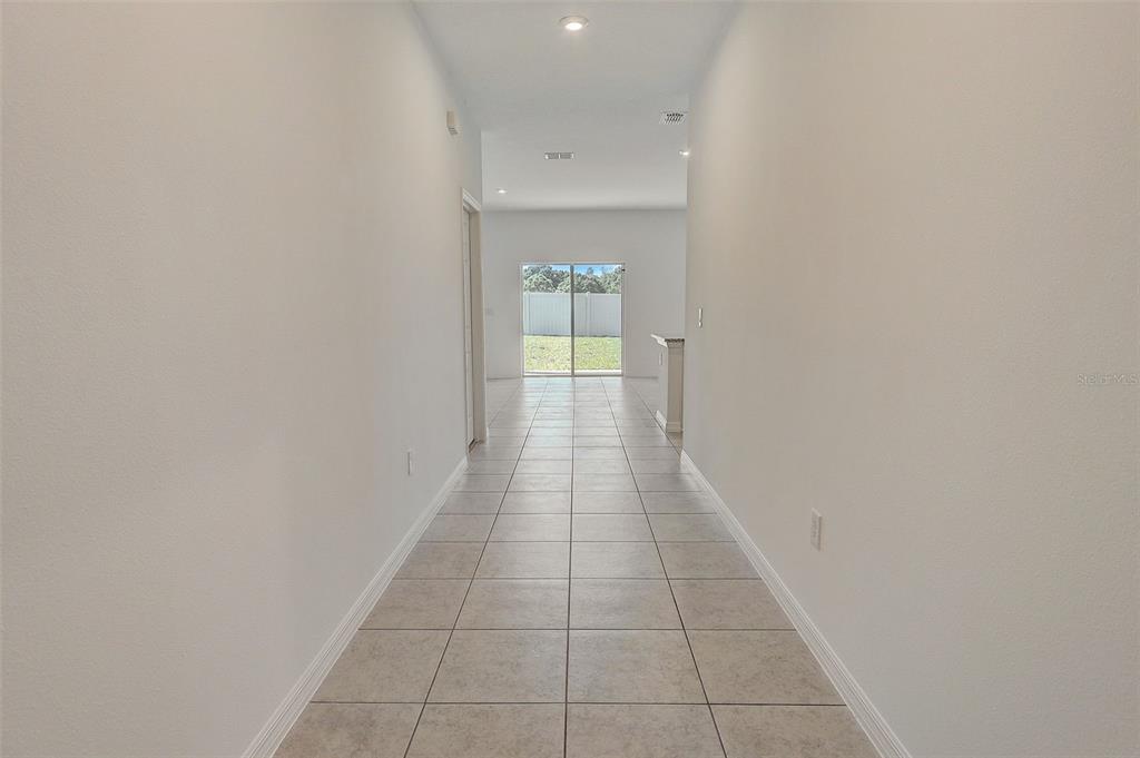 A long, tiled hallway leads toward a sliding glass door with a view of a yard — 9221 HARRIS HAWK DRIVE, LEESBURG, FL