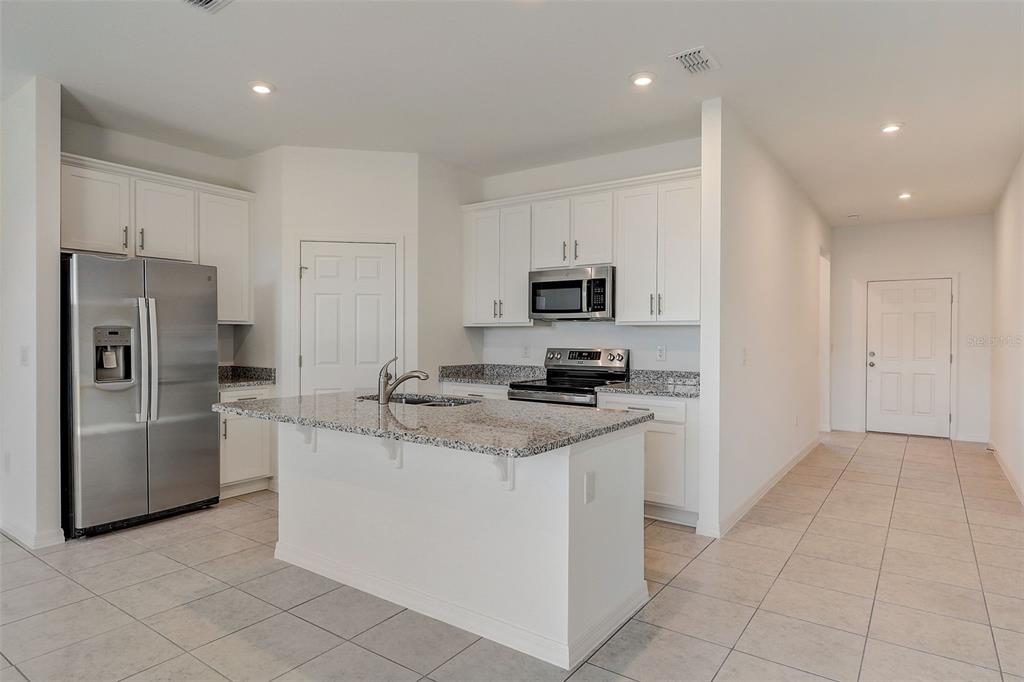 A kitchen features white cabinets, granite countertops, a stainless steel refrigerator, and tile flooring — 9221 HARRIS HAWK DRIVE, LEESBURG, FL