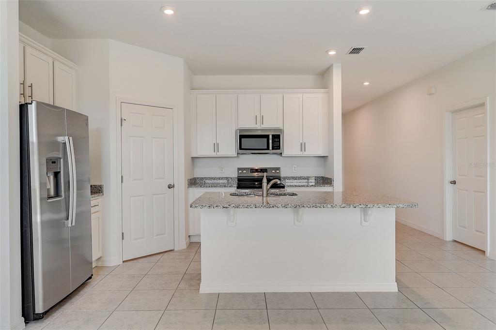 A kitchen features white cabinets, granite countertops, stainless steel appliances, and a central island — 9221 HARRIS HAWK DRIVE, LEESBURG, FL