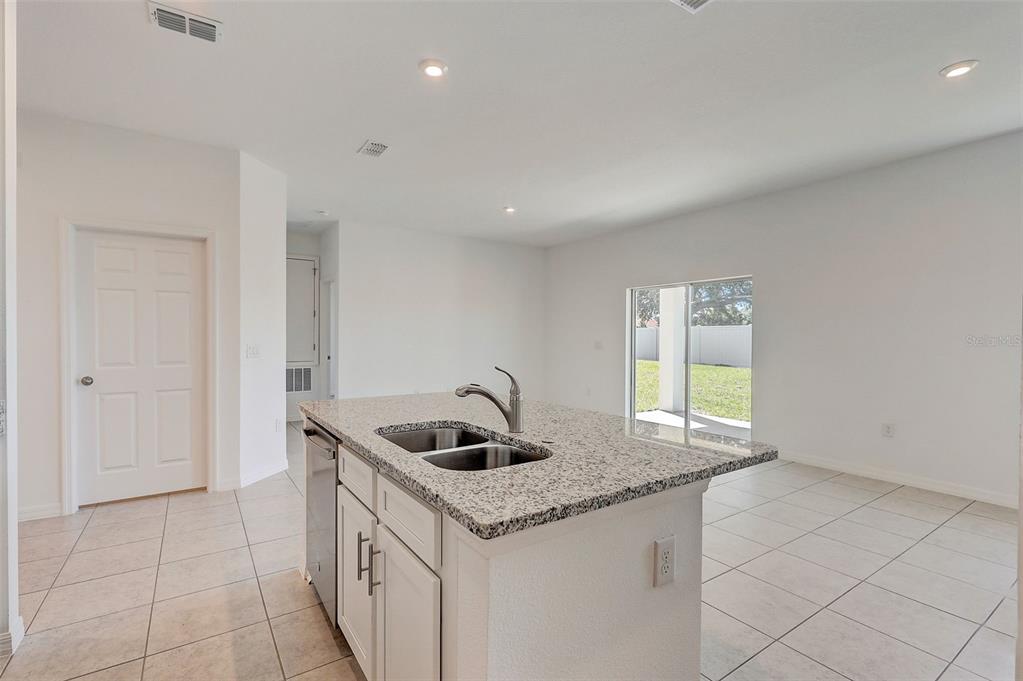 A kitchen island with a granite countertop and stainless steel sink sits in a room — 9221 HARRIS HAWK DRIVE, LEESBURG, FL