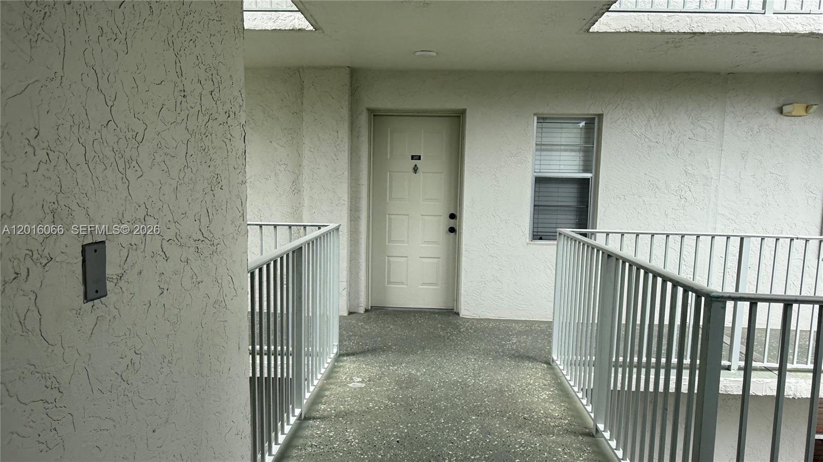 A white exterior door with the number 207 is positioned at the end of a walkway — 2236 N Cypress Bend Dr # 207, Pompano Beach FL 33069, POMPANO BEACH, FL