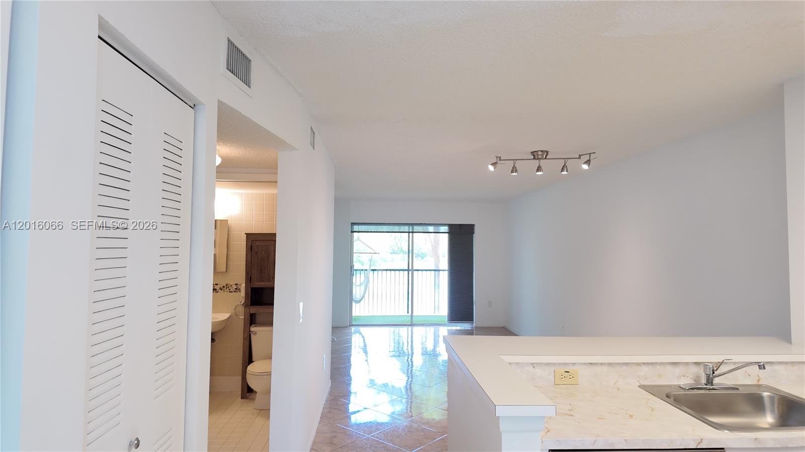 A kitchen sink and counter overlook a tiled living area with a balcony view — 2236 N Cypress Bend Dr # 207, Pompano Beach FL 33069, POMPANO BEACH, FL