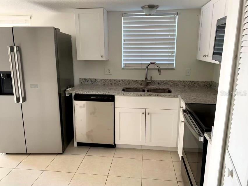 A kitchen features white cabinets, granite countertops, stainless steel appliances, and light-colored tile flooring — 5120 MYSTIC POINT COURT, ORLANDO, FL