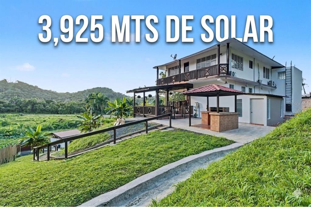 A two-story house with a covered patio and outdoor kitchen sits on a grassy hillside — Cofresi MAMEYES UNIT 57, LUQUILLO, PR