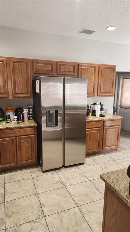 A kitchen features oak cabinets, granite countertops, a stainless steel refrigerator, and tiled flooring — 13561 HAWK LAKE DRIVE, ORLANDO, FL