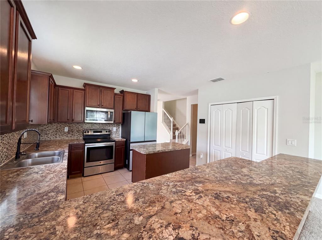A kitchen features dark wood cabinets, granite countertops, stainless steel appliances, and a center island — 4876 GRASSY KNOLL DRIVE, TAVARES, FL