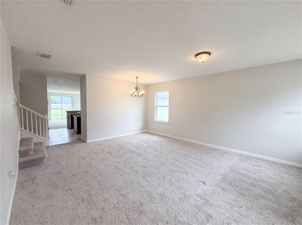 A carpeted living room features a dining area with a chandelier and a staircase — 4876 GRASSY KNOLL DRIVE, TAVARES, FL
