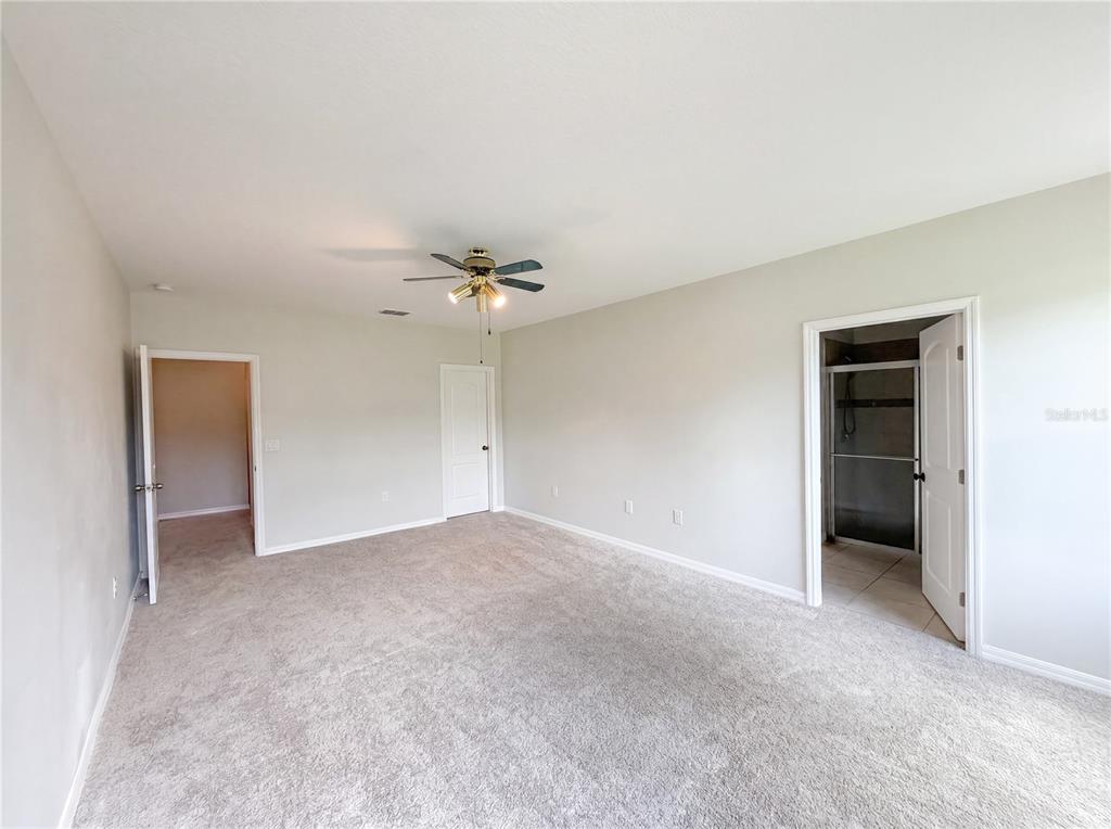 An empty bedroom with beige carpet, light walls, a ceiling fan, and three doorways — 4876 GRASSY KNOLL DRIVE, TAVARES, FL