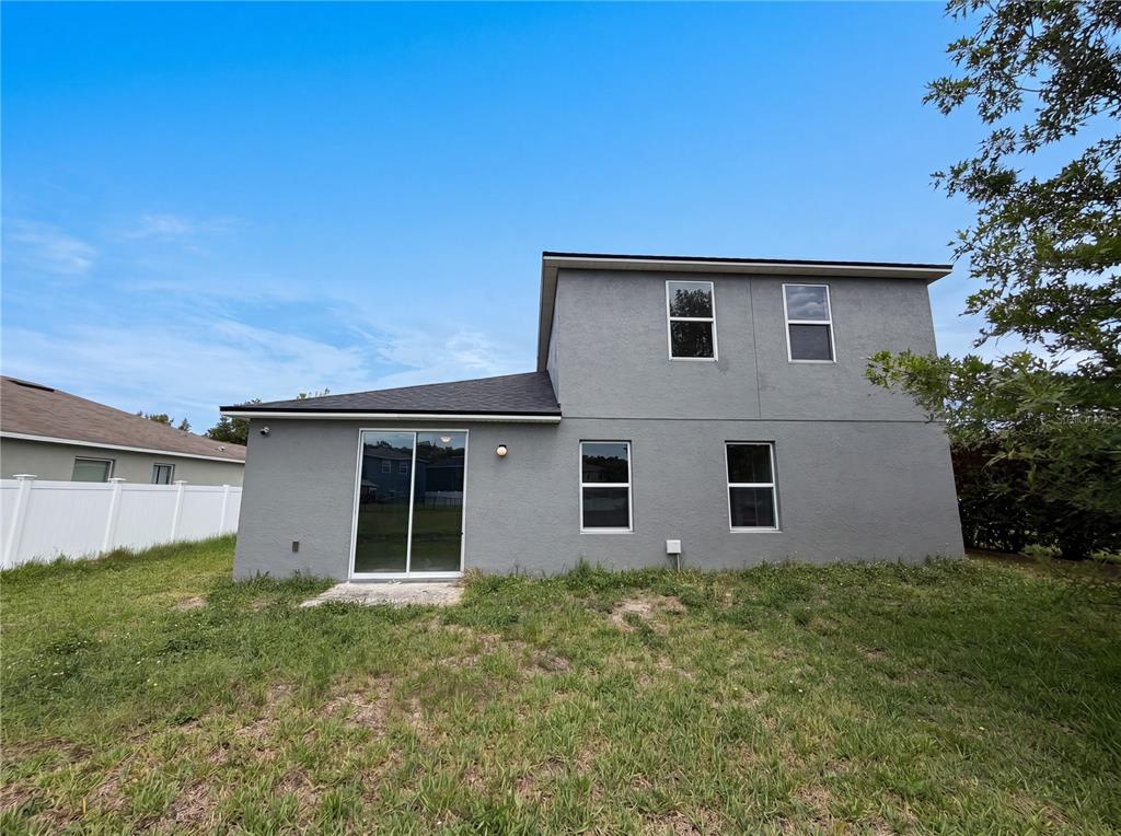 The rear exterior of a two-story gray house features a sliding glass door and windows — 4876 GRASSY KNOLL DRIVE, TAVARES, FL