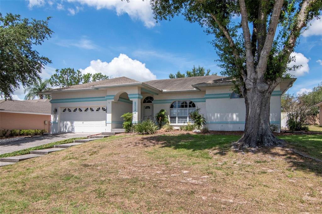 A single-story house with a white exterior, teal trim, a two-car garage, and a large tree — 5715 TANASI COURT, LAKELAND, FL