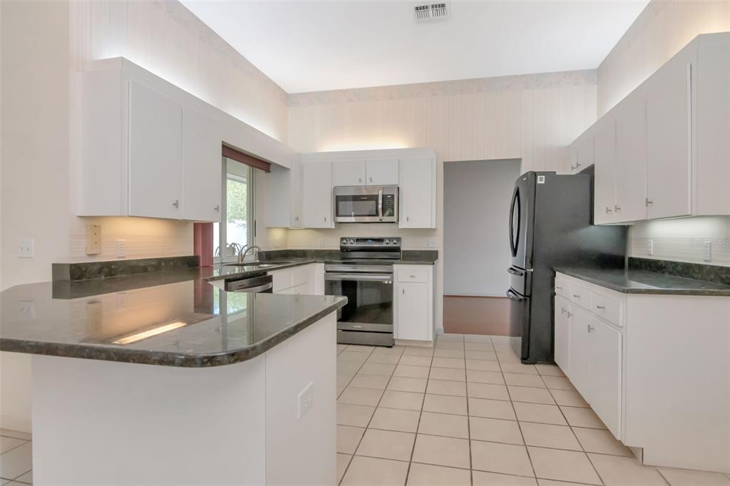 A kitchen features white cabinetry, dark countertops, stainless steel appliances, and light-colored tile flooring — 5715 TANASI COURT, LAKELAND, FL