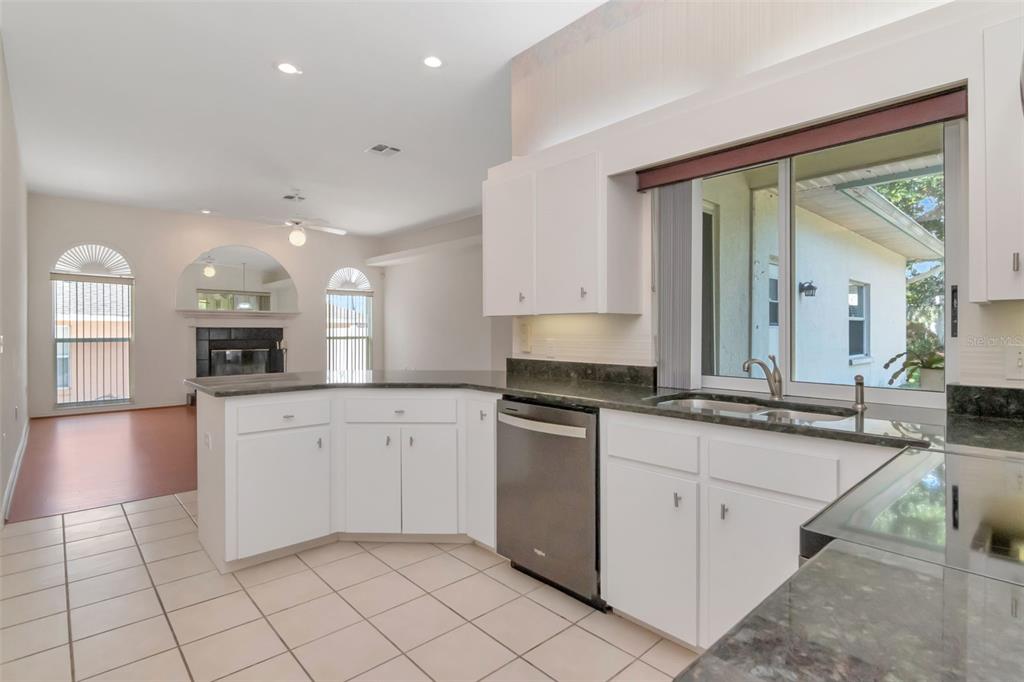 A kitchen with white cabinets, dark countertops, and tile flooring overlooks a living area — 5715 TANASI COURT, LAKELAND, FL