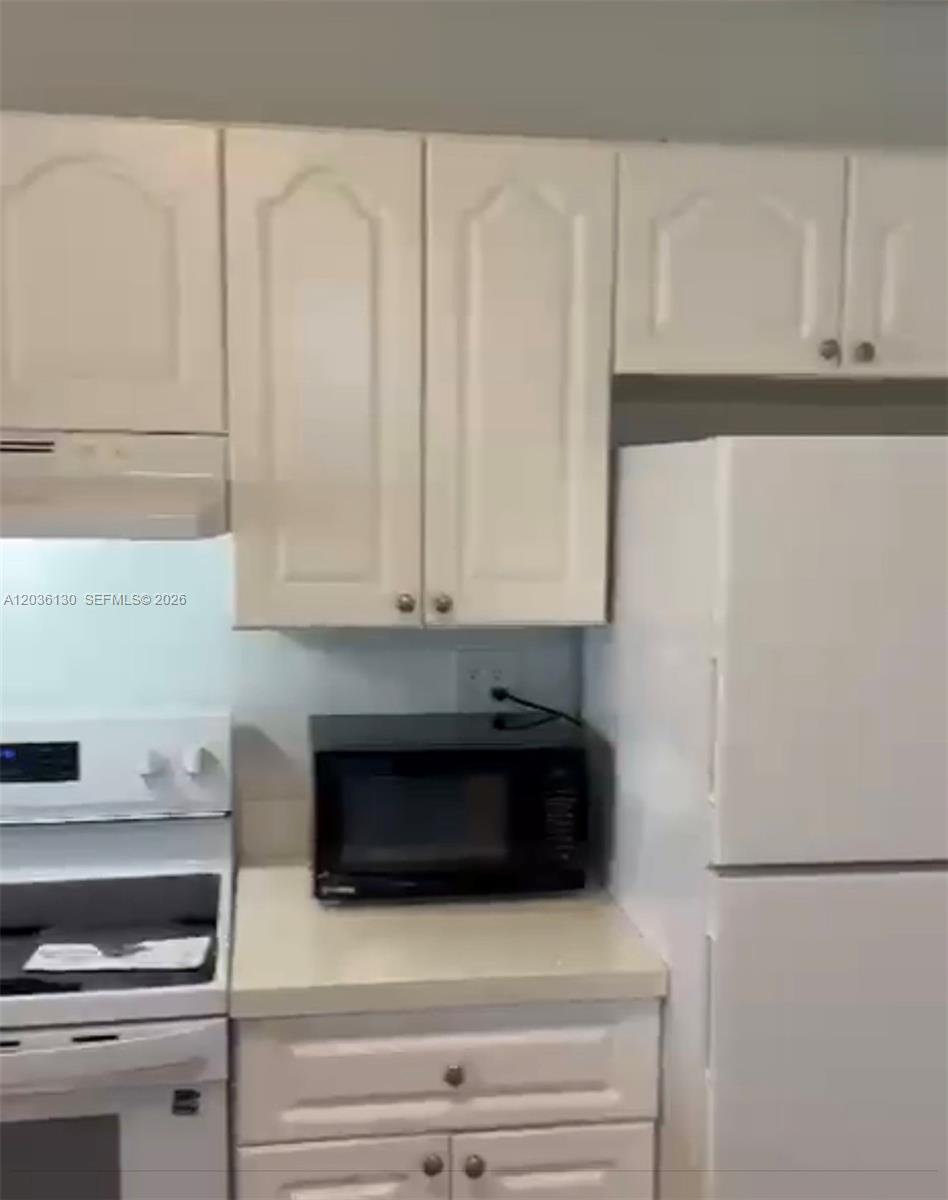 A kitchen features white cabinets, a white refrigerator, a black microwave, and a white stove — SUNRISE, FL