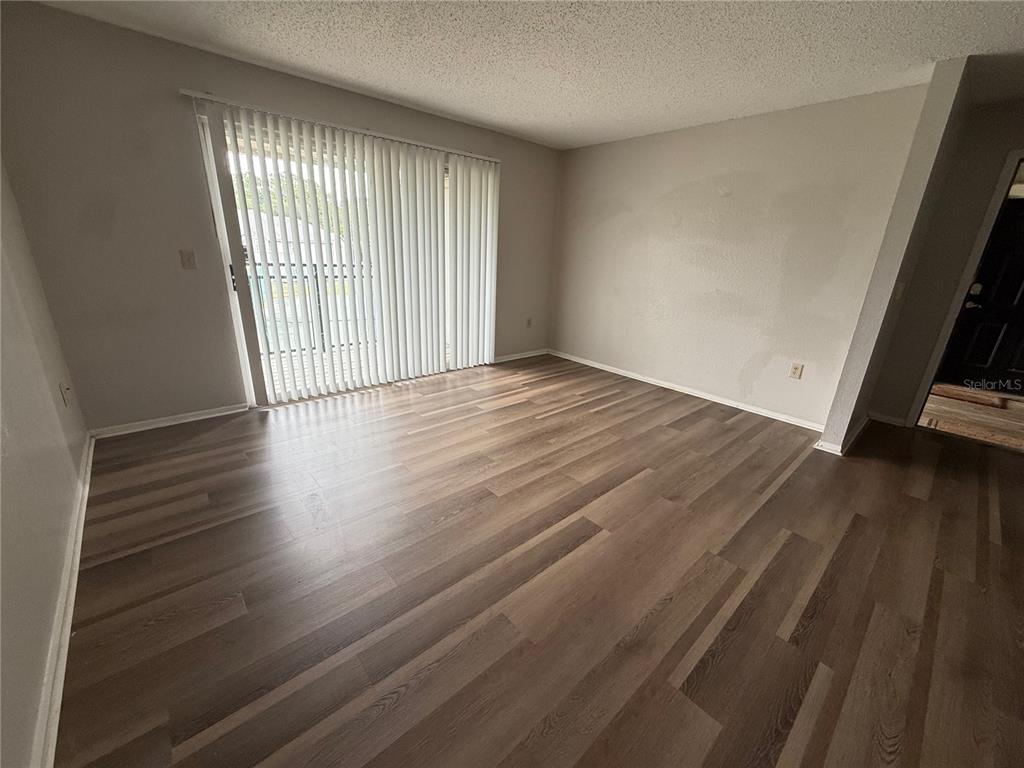 An empty living room features wood-look flooring, light-colored walls, and a sliding glass door — 3705 SW 27TH STREET UNIT 1026, GAINESVILLE, FL