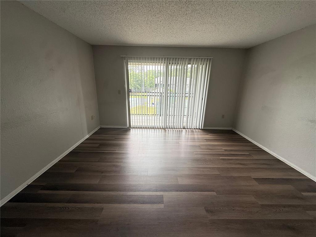 An empty room features wood-look flooring, light gray walls, and a sliding glass door — 3705 SW 27TH STREET UNIT 1026, GAINESVILLE, FL